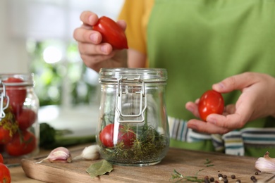 Photo of Woman putting tomatoes into pickling jar at table in kitchen, closeup