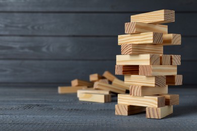 Photo of Jenga tower made of wooden blocks on grey table, space for text