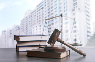 Wooden gavel, scales of justice and books on table against beautiful cityscape 