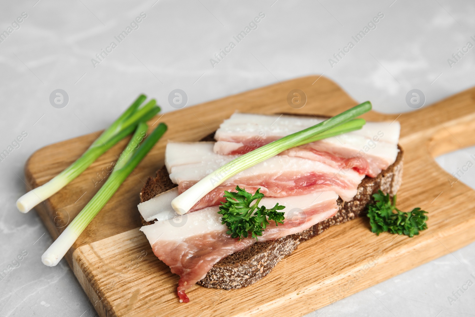 Photo of Board with pork fatback sandwich and onions on grey stone background