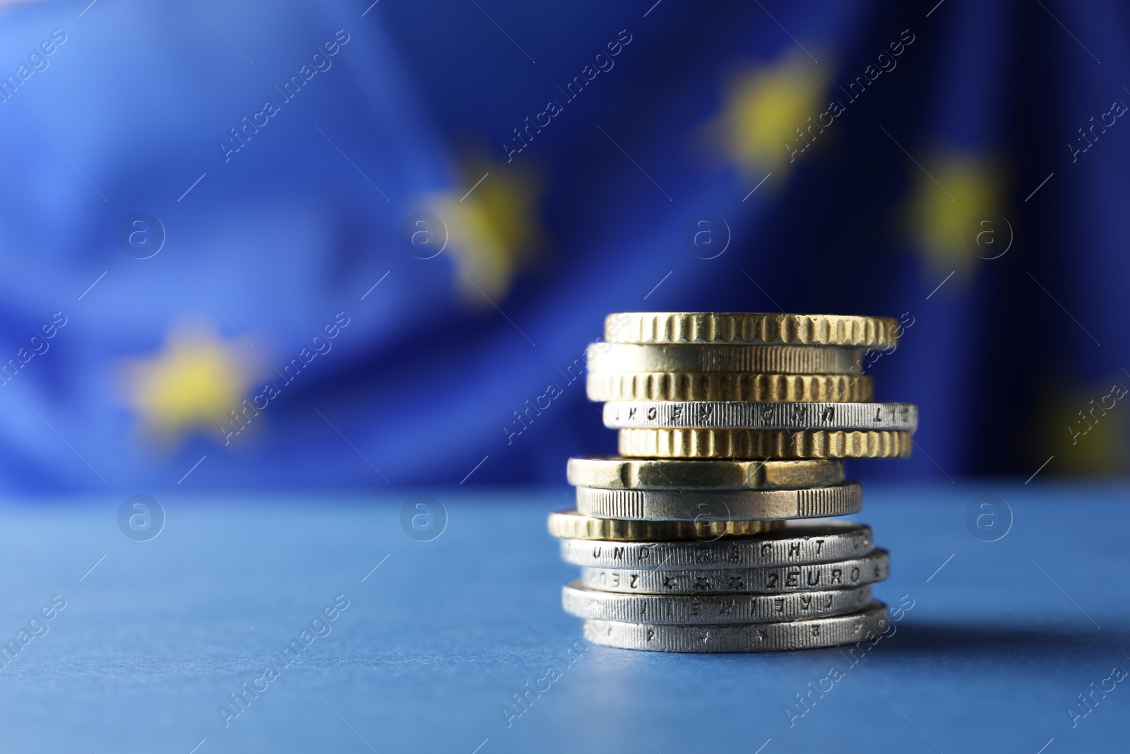 Photo of Stack of coins on blue table against European Union flag, closeup. Space for text