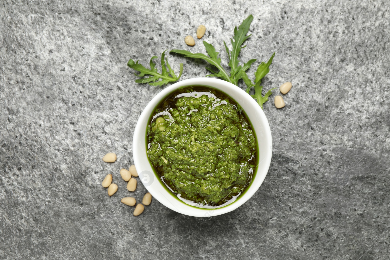 Photo of Bowl of tasty arugula pesto and ingredients on grey table, flat lay