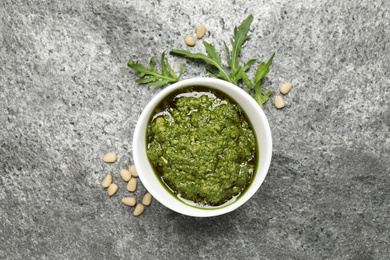 Photo of Bowl of tasty arugula pesto and ingredients on grey table, flat lay