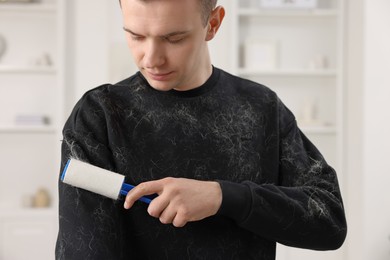 Pet shedding. Man with lint roller removing dog's hair from sweater at home