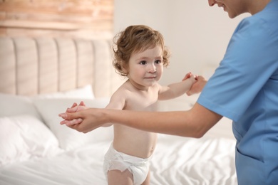 Orthopedist examining little baby on bed indoors