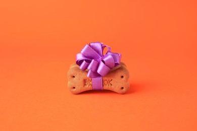 Photo of Bone shaped dog cookies with purple bow on orange background