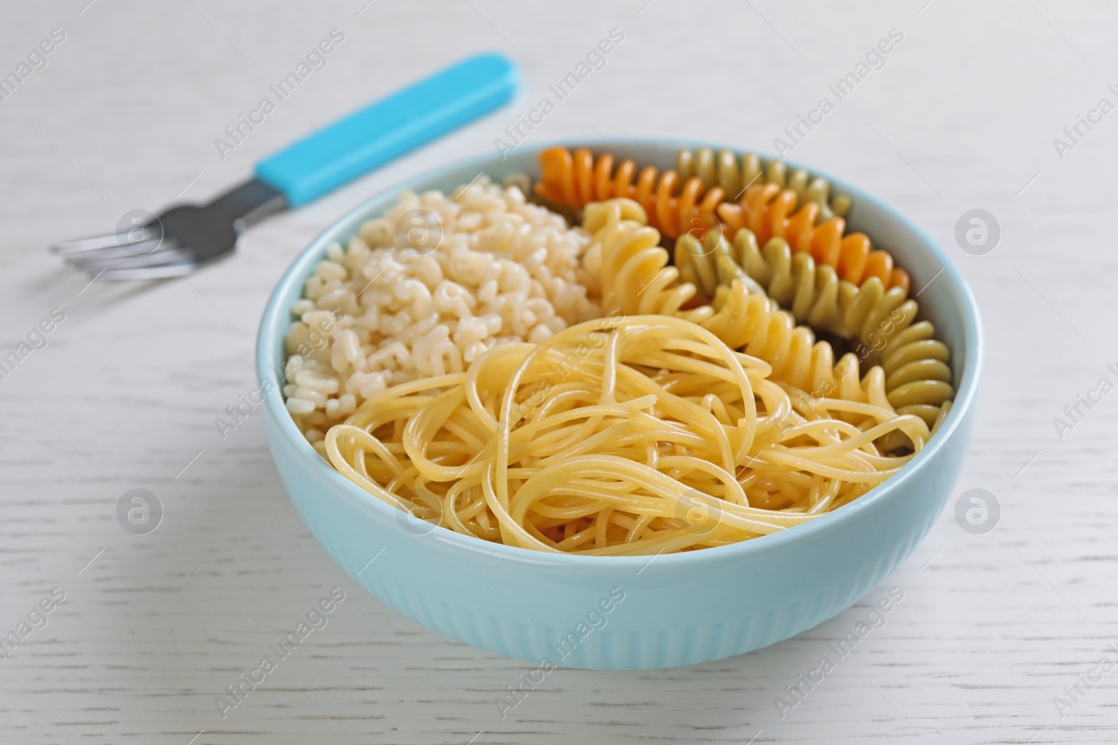 Photo of Bowl with different types of tasty pasta on white wooden table