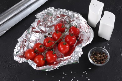 Tomatoes in aluminum foil and spices on dark textured table, above view