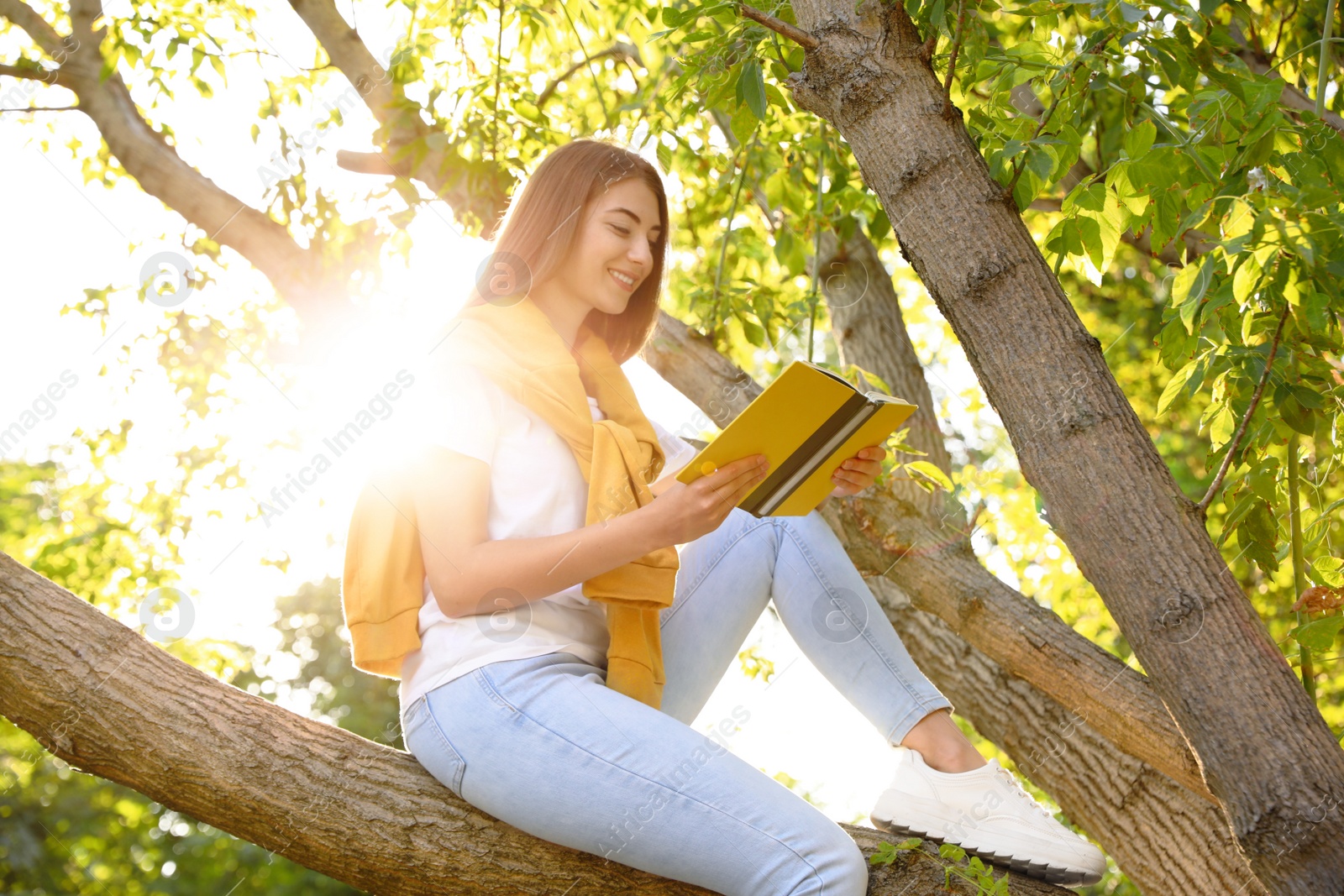 Photo of Young woman reading book on tree in park