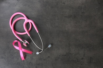 Photo of Pink ribbon and stethoscope on dark background, top view with space for text. Breast cancer concept