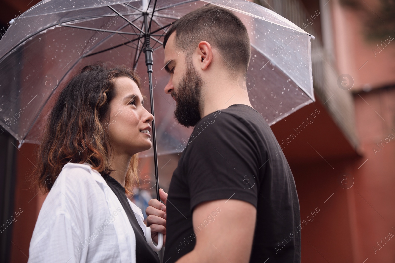 Photo of Young couple with umbrella enjoying time together under rain on city street