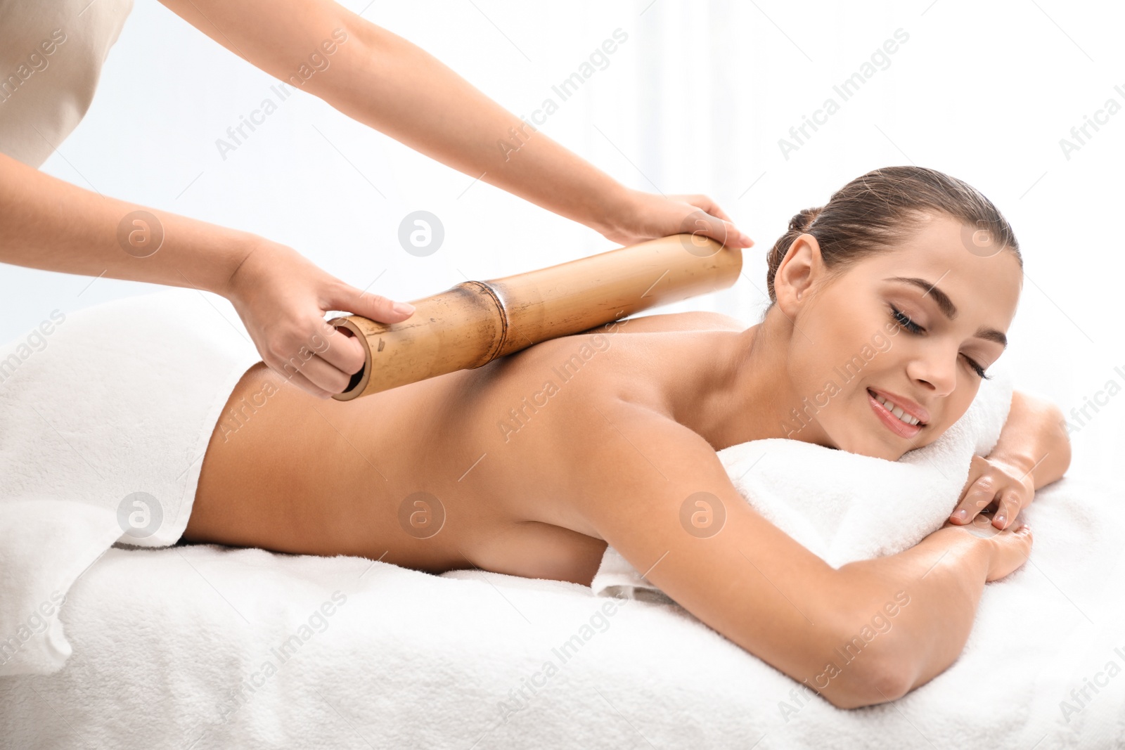 Photo of Young woman having massage with bamboo stick in wellness center