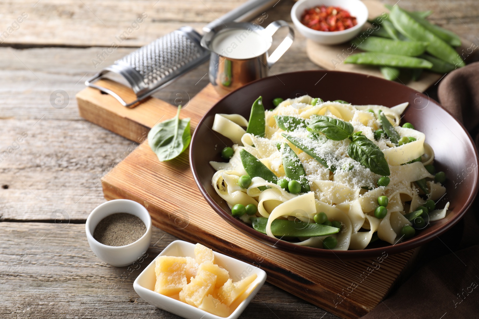 Photo of Delicious pasta with green peas and ingredients on wooden table