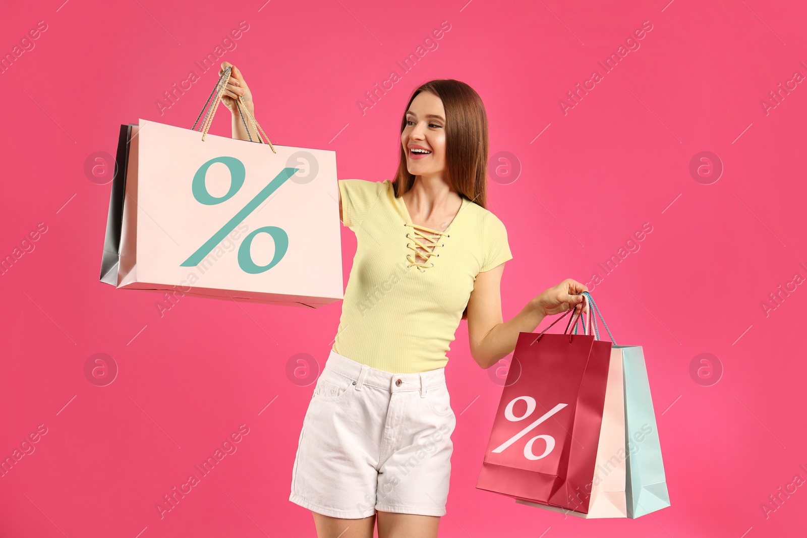 Image of Happy woman holding paper shopping bags with percent signs on pink background. Discount concept