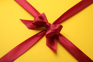 Photo of Red satin ribbon with bow on yellow background