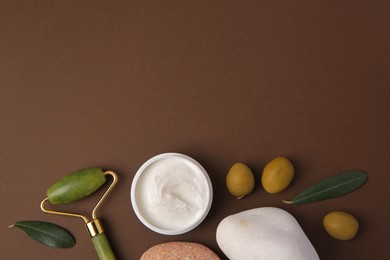 Photo of Flat lay composition with jar of cream, face roller and stones on brown background. Space for text