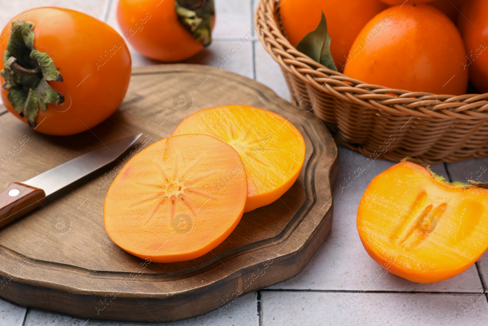 Photo of Delicious ripe juicy persimmons and knife on wooden board, closeup