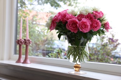 Photo of Vase with beautiful bouquet of roses and candles on windowsill indoors