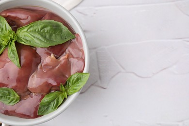 Bowl with raw chicken liver and basil on white textured table, top view. Space for text