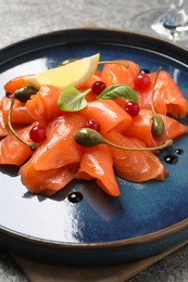 Photo of Salmon carpaccio with capers, cranberries, basil and lemon on grey table, closeup