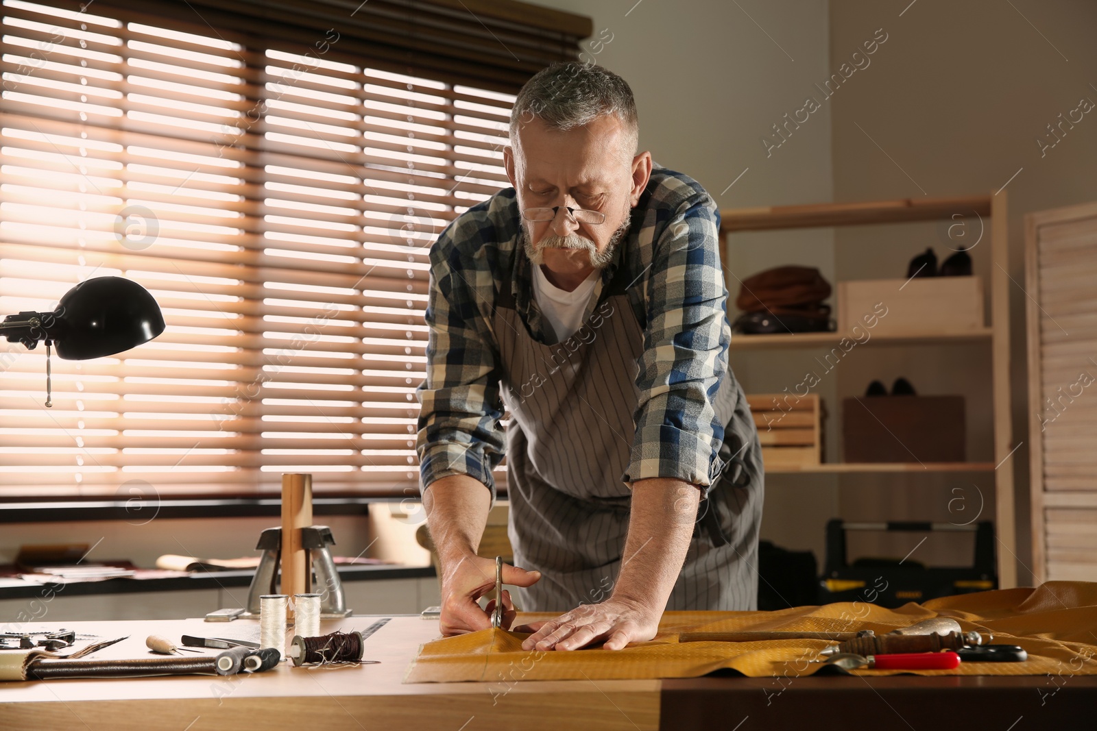 Photo of Man cutting leather with scissors in workshop