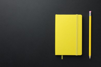 Closed yellow notebook and pencil on black background, top view. Space for text