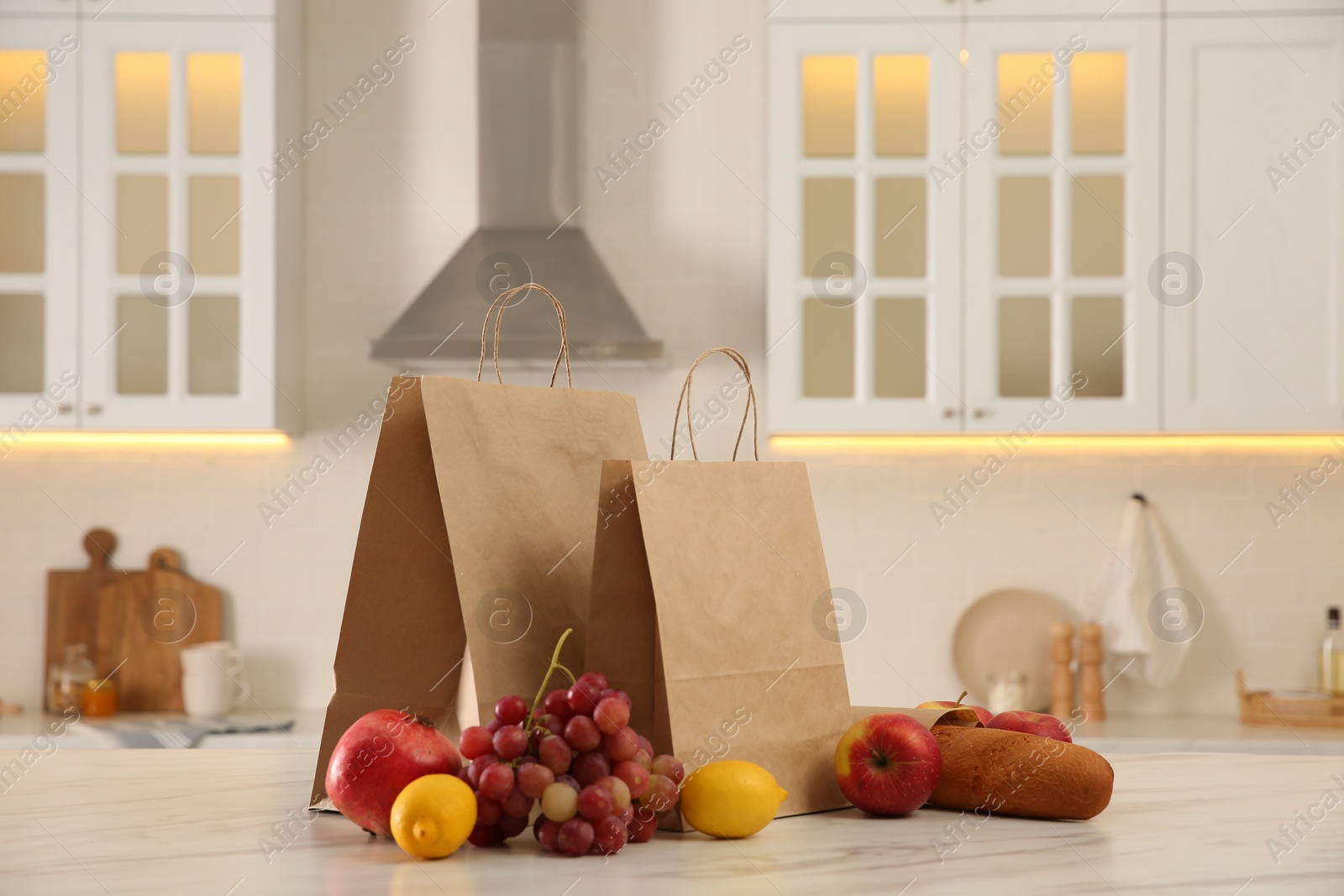 Photo of Paper shopping bags and fresh fruits on white marble table in kitchen
