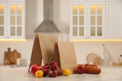 Paper shopping bags and fresh fruits on white marble table in kitchen