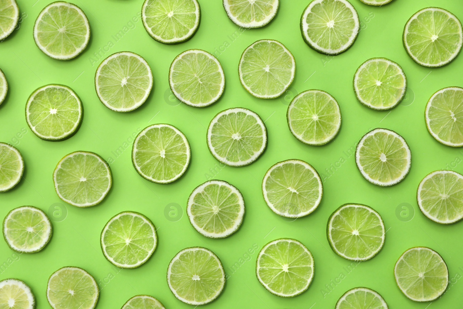 Photo of Slices of fresh juicy limes on green background, flat lay