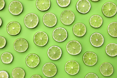 Photo of Slices of fresh juicy limes on green background, flat lay