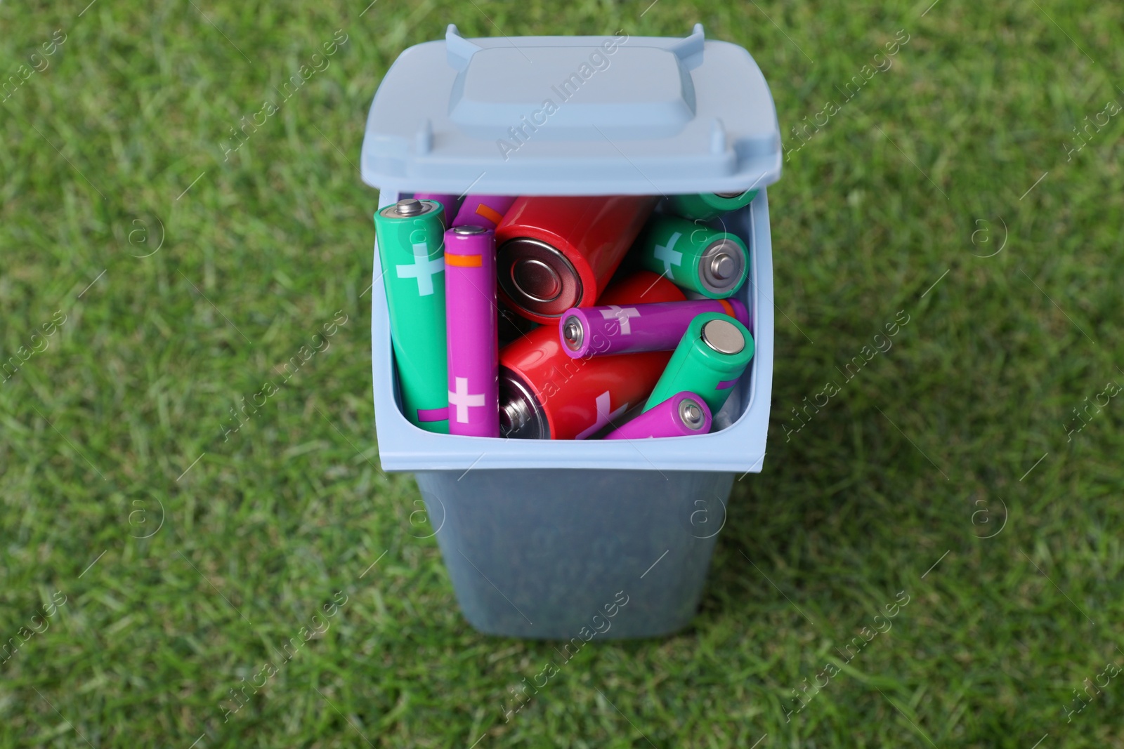 Photo of Many used batteries in recycling bin on green grass