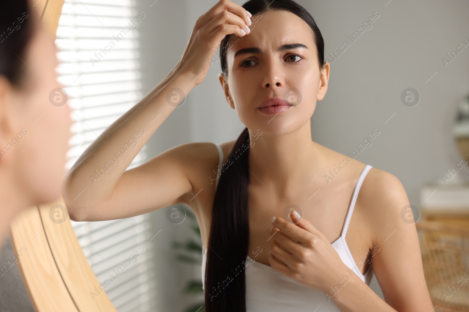 Photo of Woman with dry skin looking at mirror in bathroom