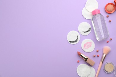 Photo of Dirty cotton pads, cosmetic products and micellar cleansing water on lilac background, flat lay. Space for text