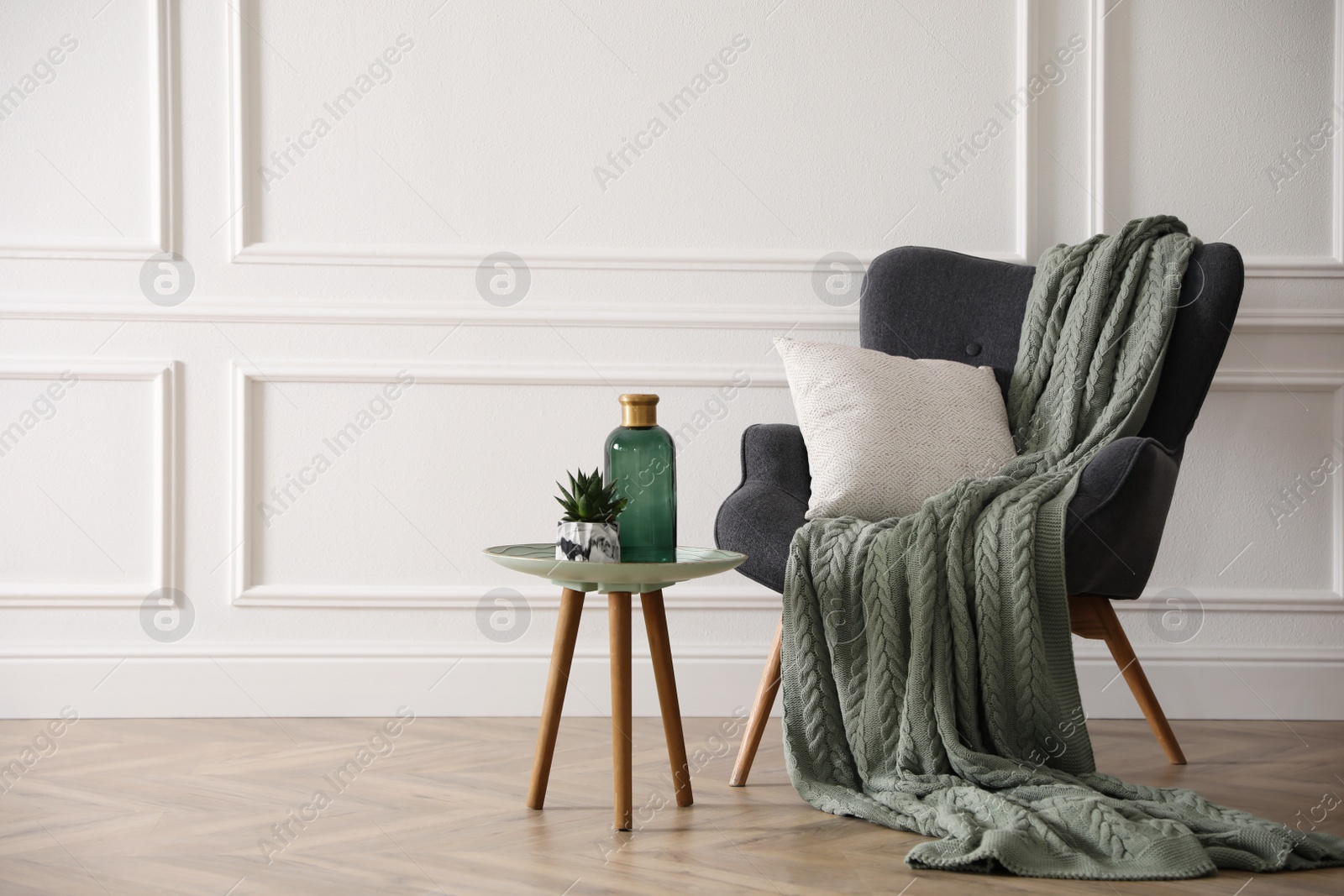 Photo of Modern armchair with knitted blanket and cushion in stylish room interior. Space for text