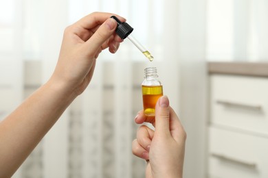 Photo of Woman holding bottle of hemp oil and pipette on blurred background, closeup