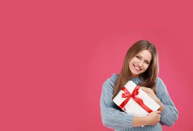 Photo of Happy young woman with Christmas gift on pink background. Space for text