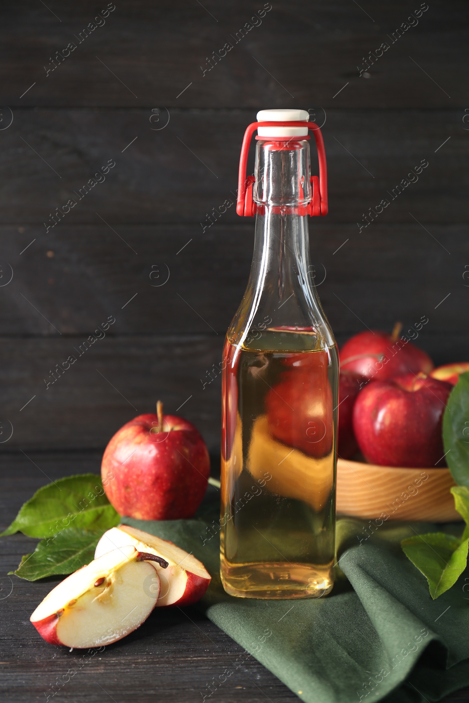 Photo of Bottle of delicious cider, cut and whole apples with green leaves on black wooden table