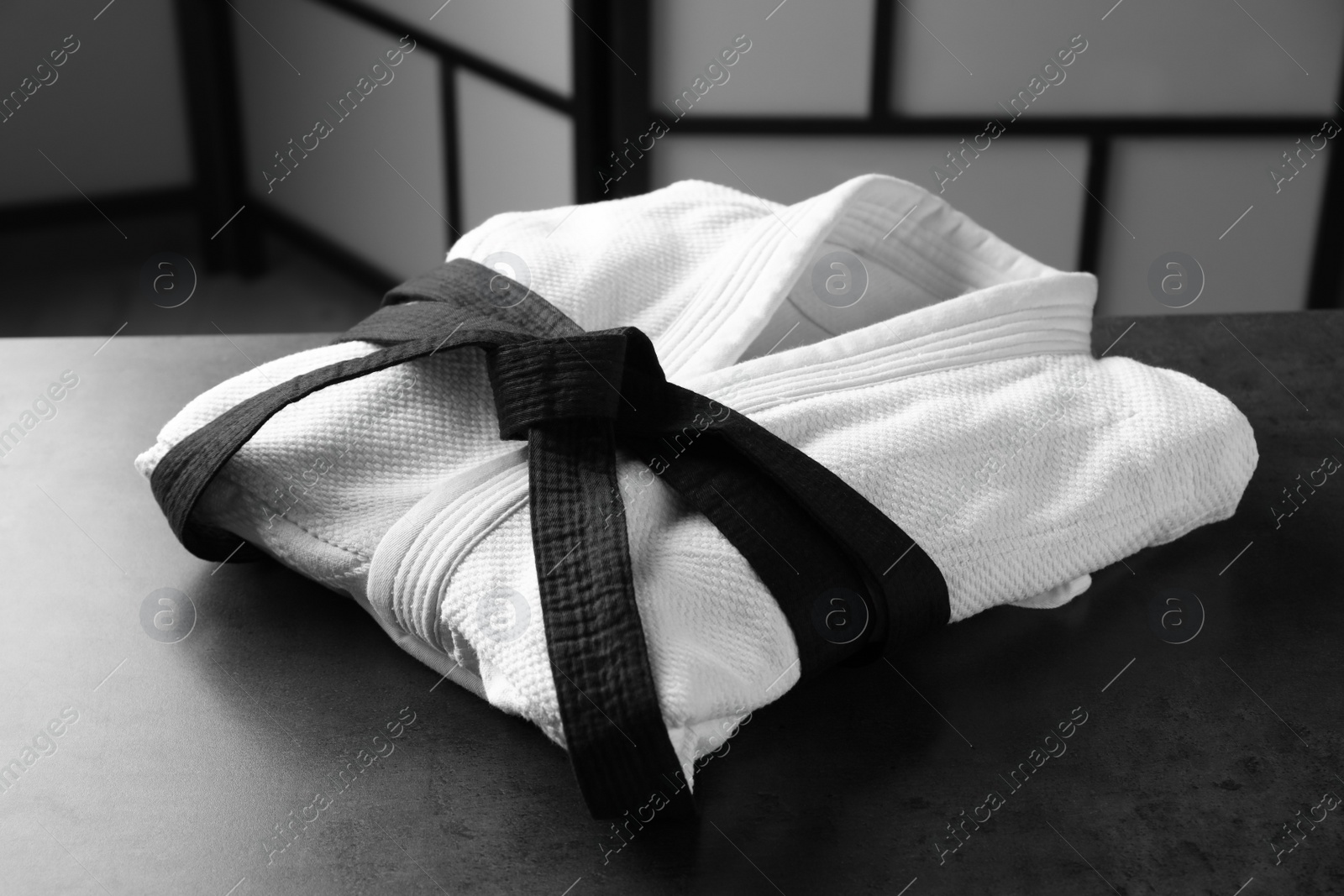 Photo of Martial arts uniform with black belt on grey stone table indoors