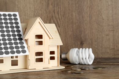 Photo of Wooden house model with solar panels, lightbulb and coins on table