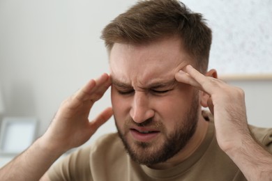 Photo of Young man suffering from migraine at home