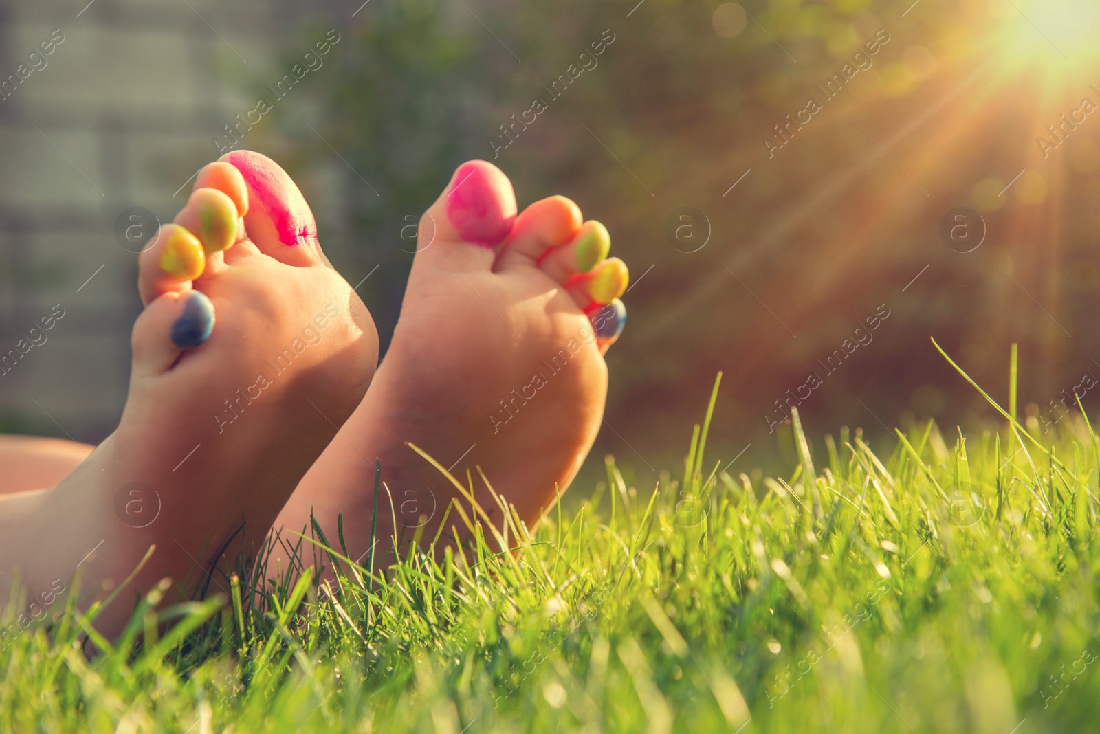 Photo of Teenage girl with painted toes on green grass outdoors, closeup. Space for text