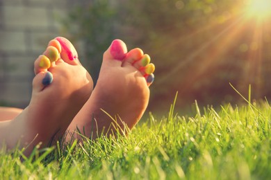 Teenage girl with painted toes on green grass outdoors, closeup. Space for text