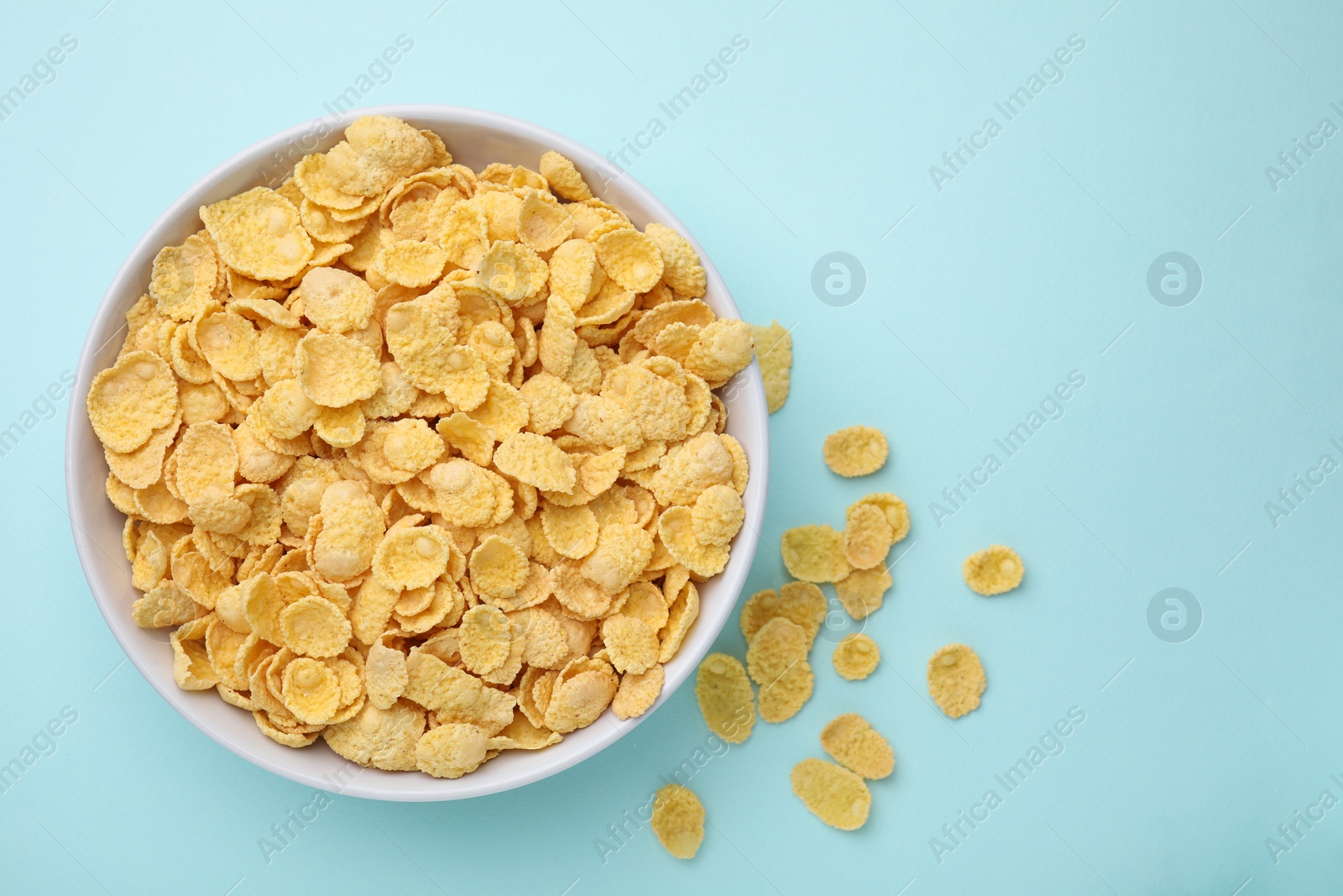 Photo of Breakfast cereal. Tasty corn flakes in bowl on light blue table, top view. Space for text