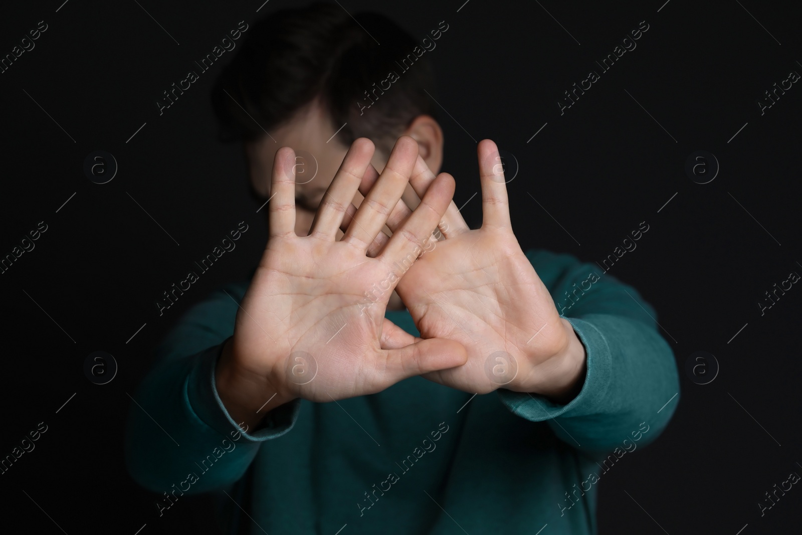 Photo of Man showing stop gesture against black background, focus on hands