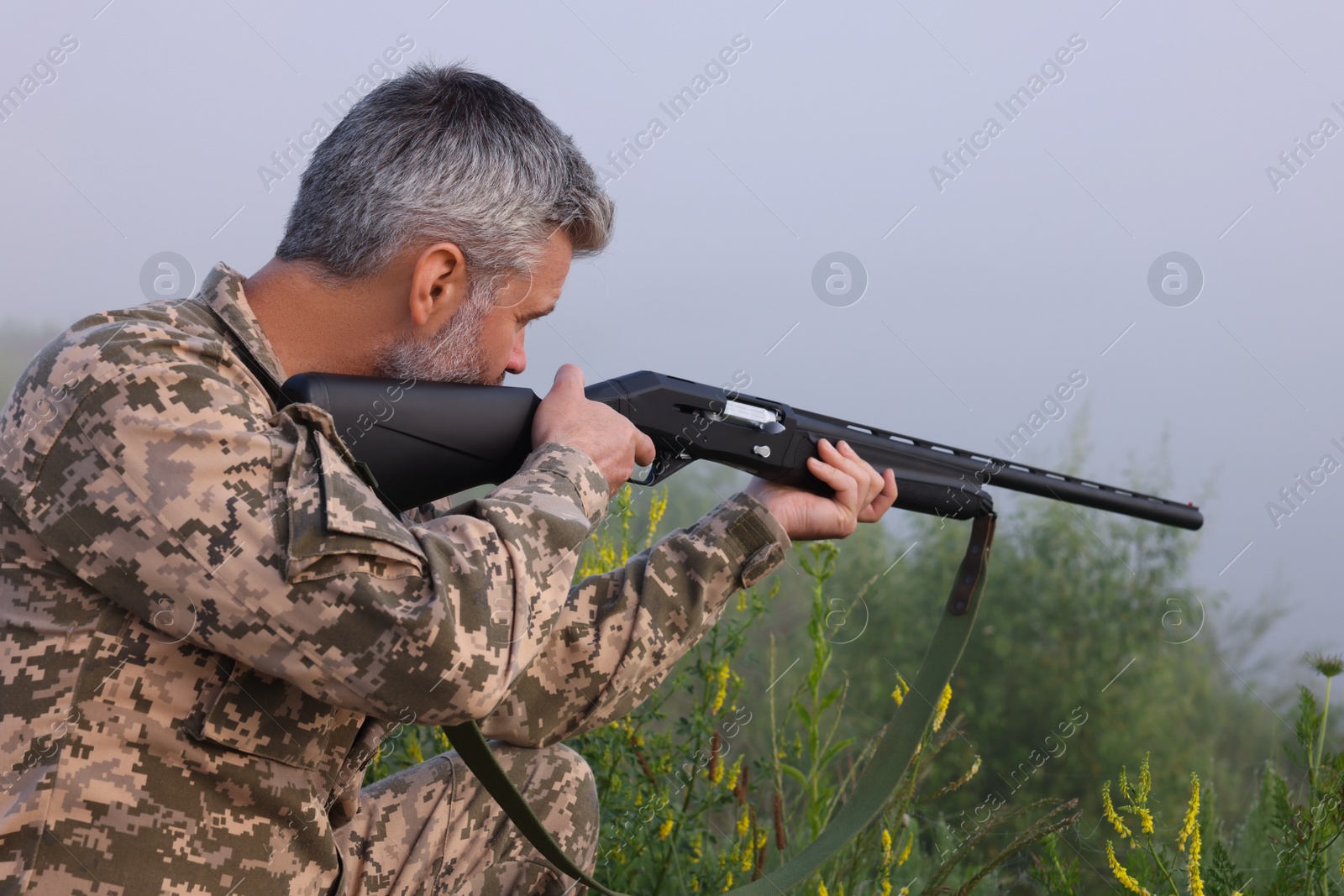 Photo of Man wearing camouflage and aiming with hunting rifle outdoors
