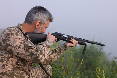 Man wearing camouflage and aiming with hunting rifle outdoors