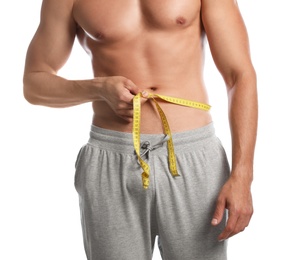 Young man with slim body using measuring tape on white background, closeup view