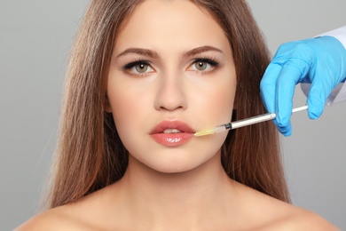 Young woman getting lips injection on grey background. Cosmetic surgery