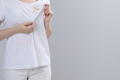 Woman showing stain on her t-shirt against light grey background, closeup. Space for text