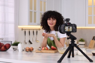 Photo of Smiling food blogger explaining something while recording video in kitchen